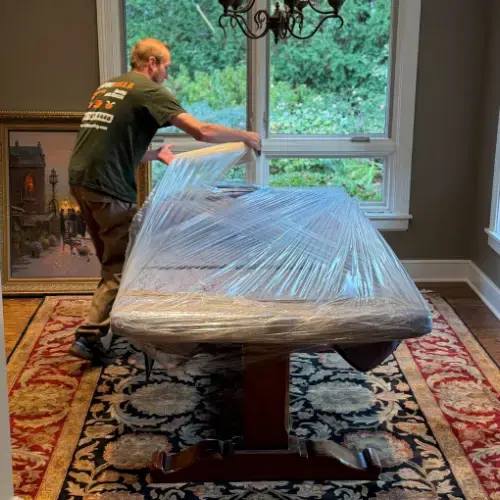 Mover wrapping a dining table with stretch wrap in a well-lit home