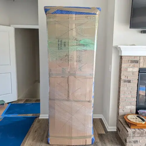 Glass display cabinet fully wrapped with cardboard, blankets, and stretch wrap