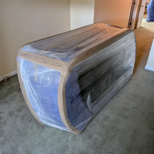 Sofa wrapped in blankets, cardboard, and stretch wrap lying on carpeted floor