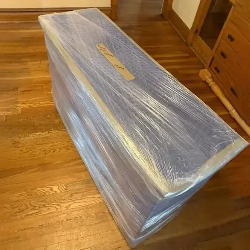 Furniture piece wrapped in moving blankets and stretch wrap on hardwood floor