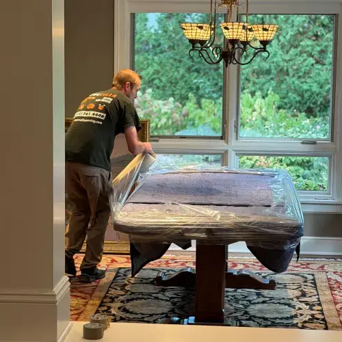 Mover securing a dining table with moving blankets and stretch wrap