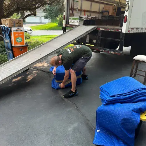 Mover folding blue blankets beside a moving truck ramp