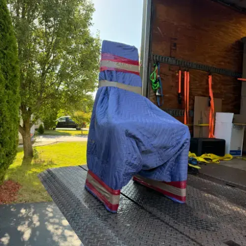 Chair fully wrapped in blue moving blankets and secured with red tape on truck liftgate