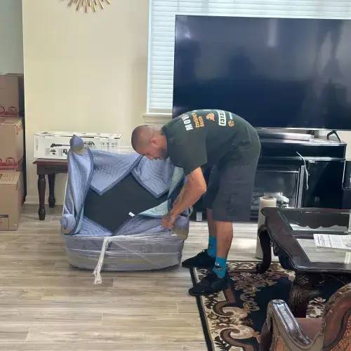Mover wrapping an armchair with blankets and plastic film in living room