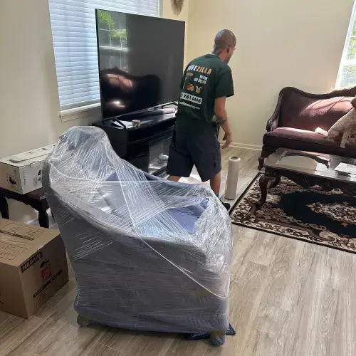 Mover standing near a wrapped armchair in a bright living room