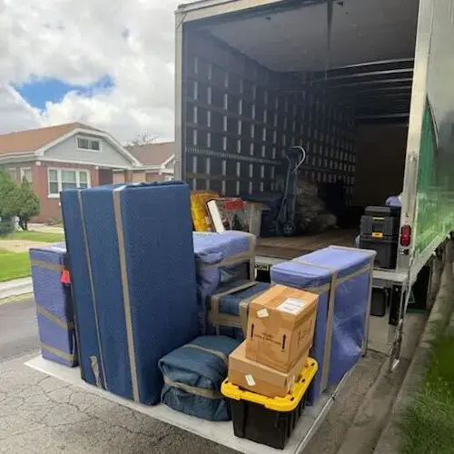 Partially loaded moving truck with wrapped furniture and boxes on liftgate